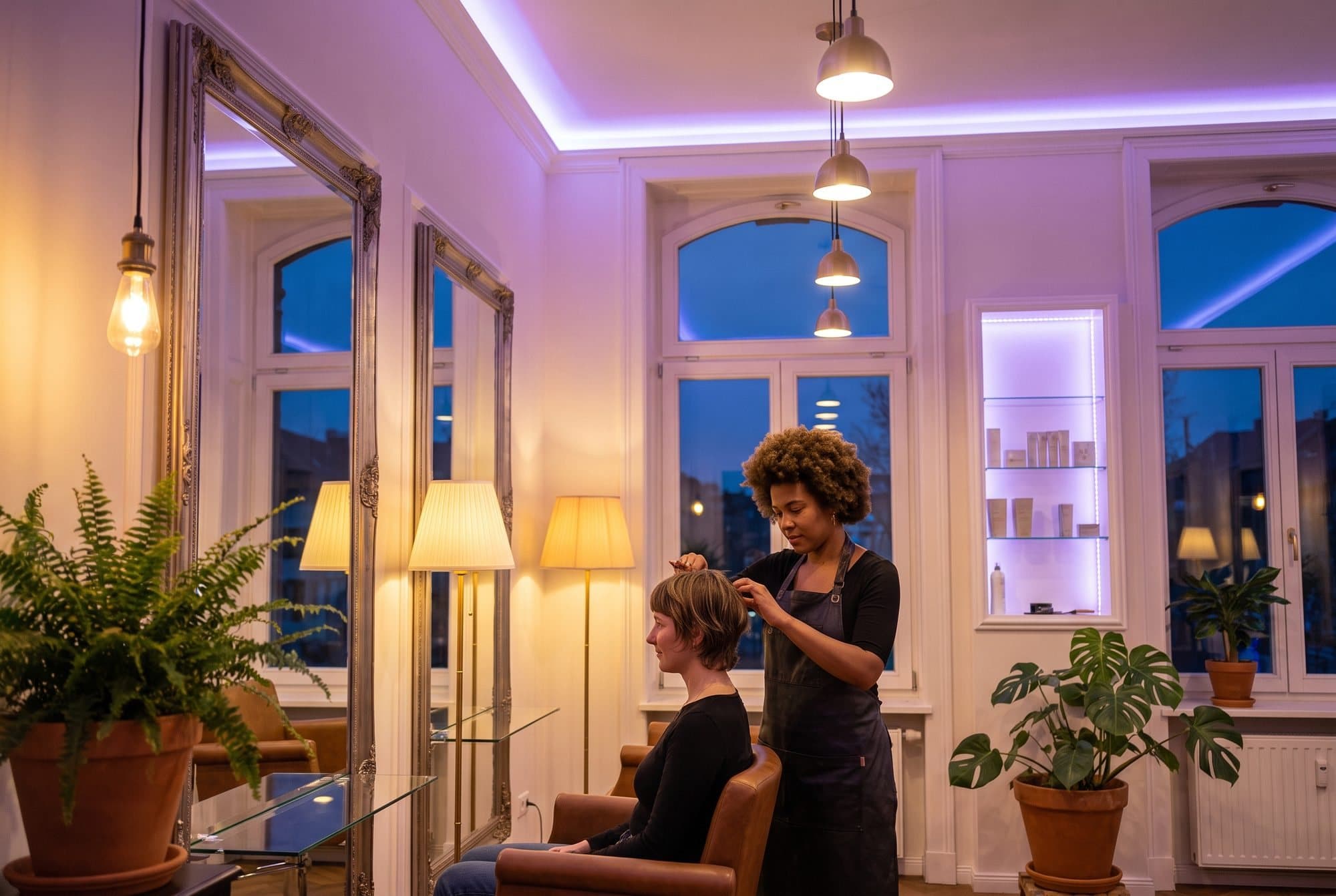 Frizerka uređuje kosu klijentici u svijetlom salonu s biljkama